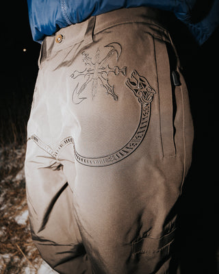 Brown pants with intricate designs worn by a person in a dark setting